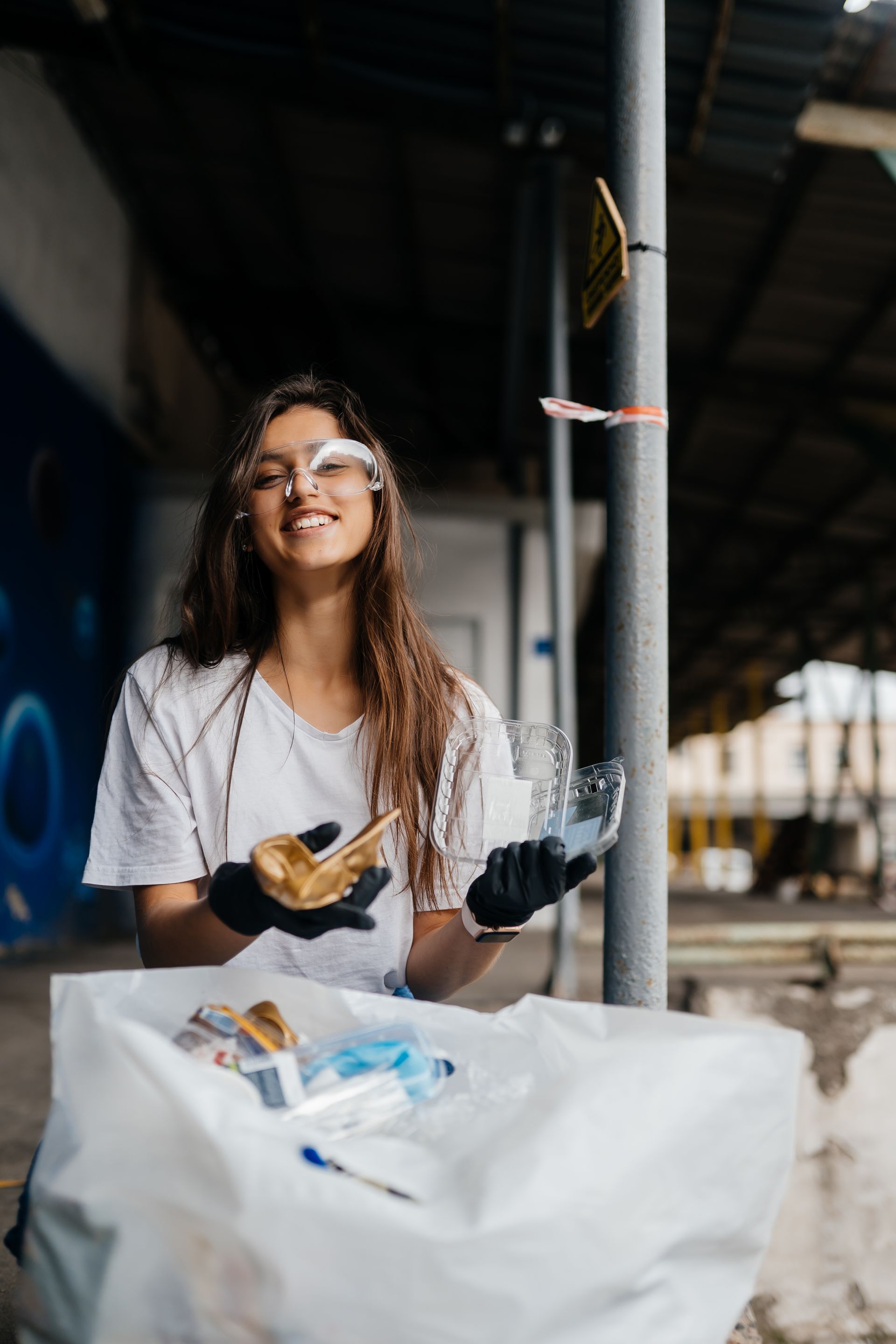 A woman is standing next to a trash can holding a plastic bottle.