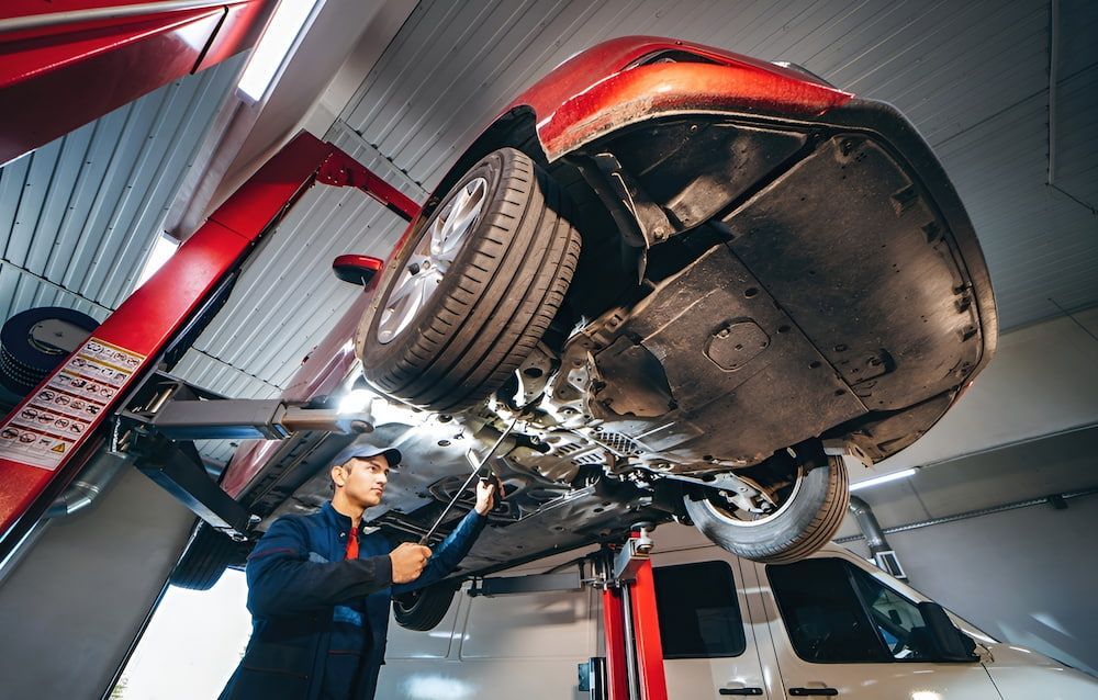 A Man Is Working On A Car On A Lift In A Garage — Mullumbimby Automotive in Mullumbimby, NSW