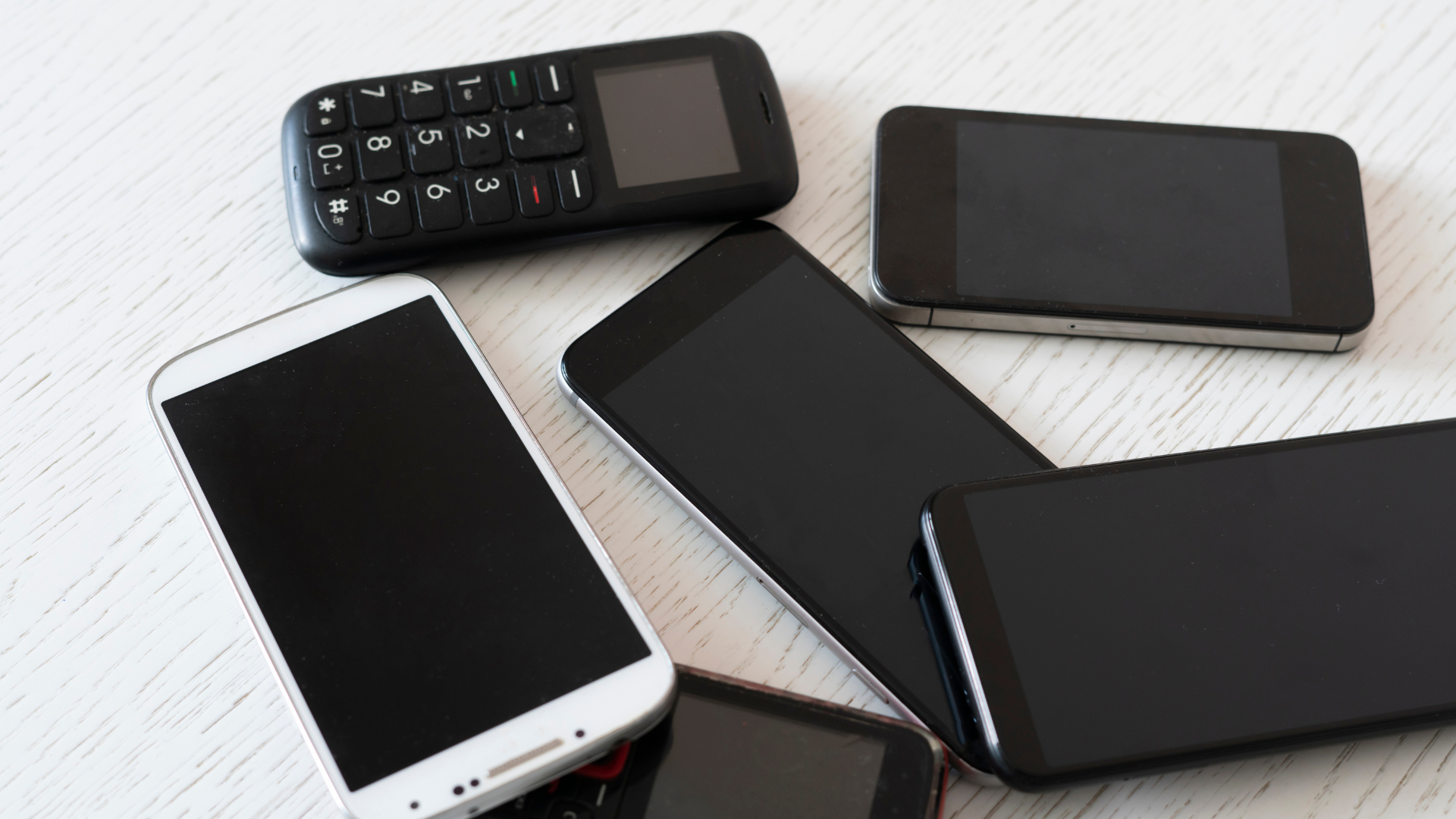 A bunch of cell phones are laying on a table.