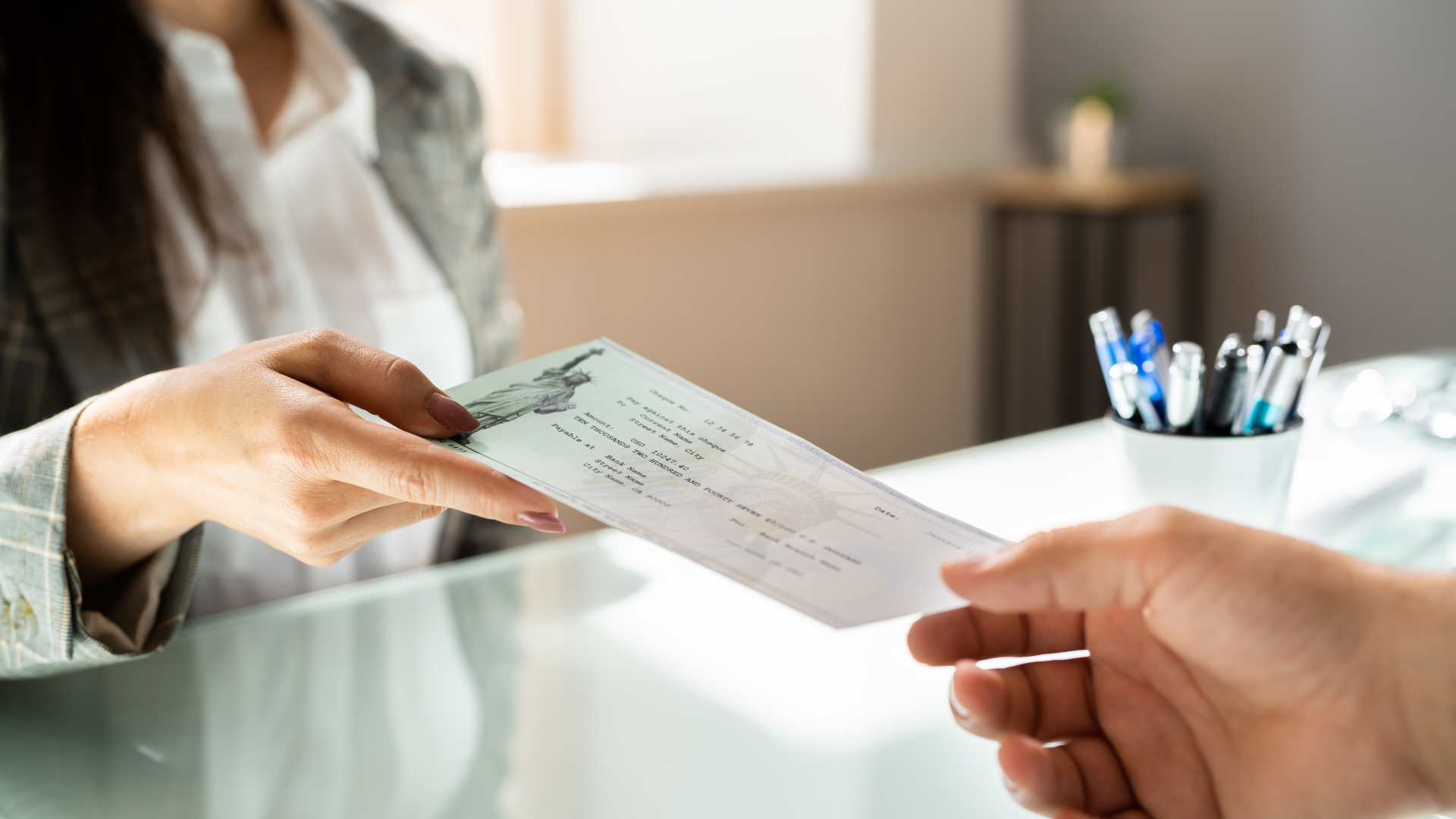 A man is handing a check to a woman at a desk.
