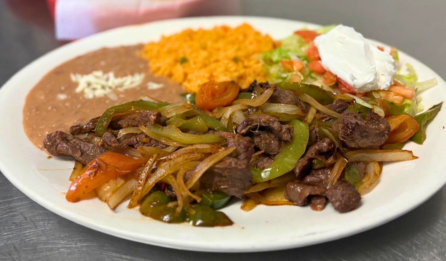 Steak fajitas sizzling with peppers, onions, rice, and beans