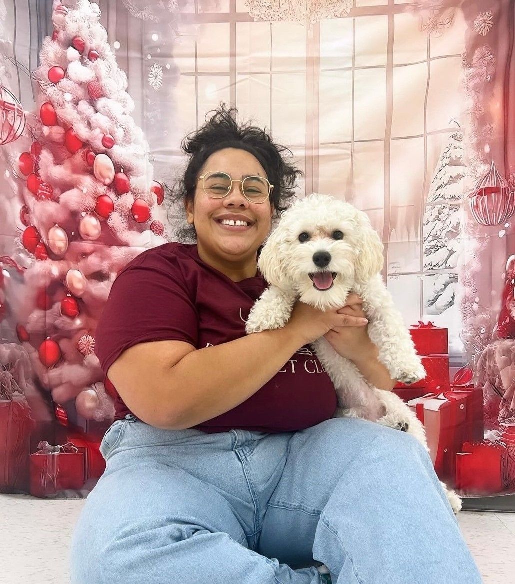 Zoe is holding a small white dog in front of a Christmas tree 