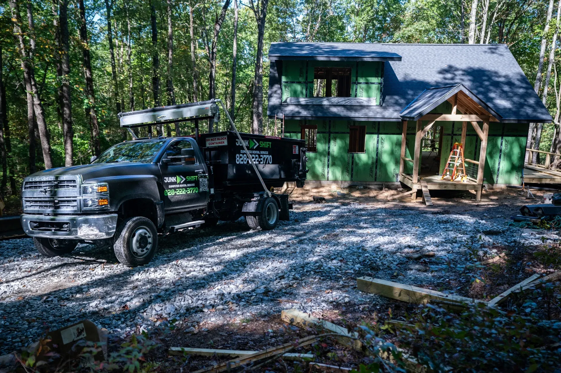 A green dumpster is sitting on top of a gravel road.