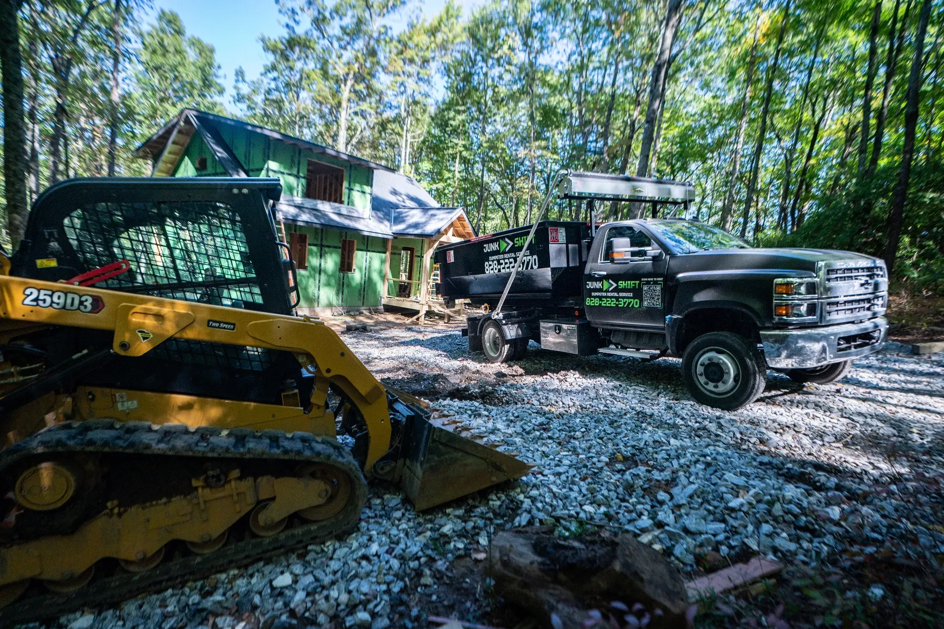 A row of dumpsters are parked in a gravel lot.