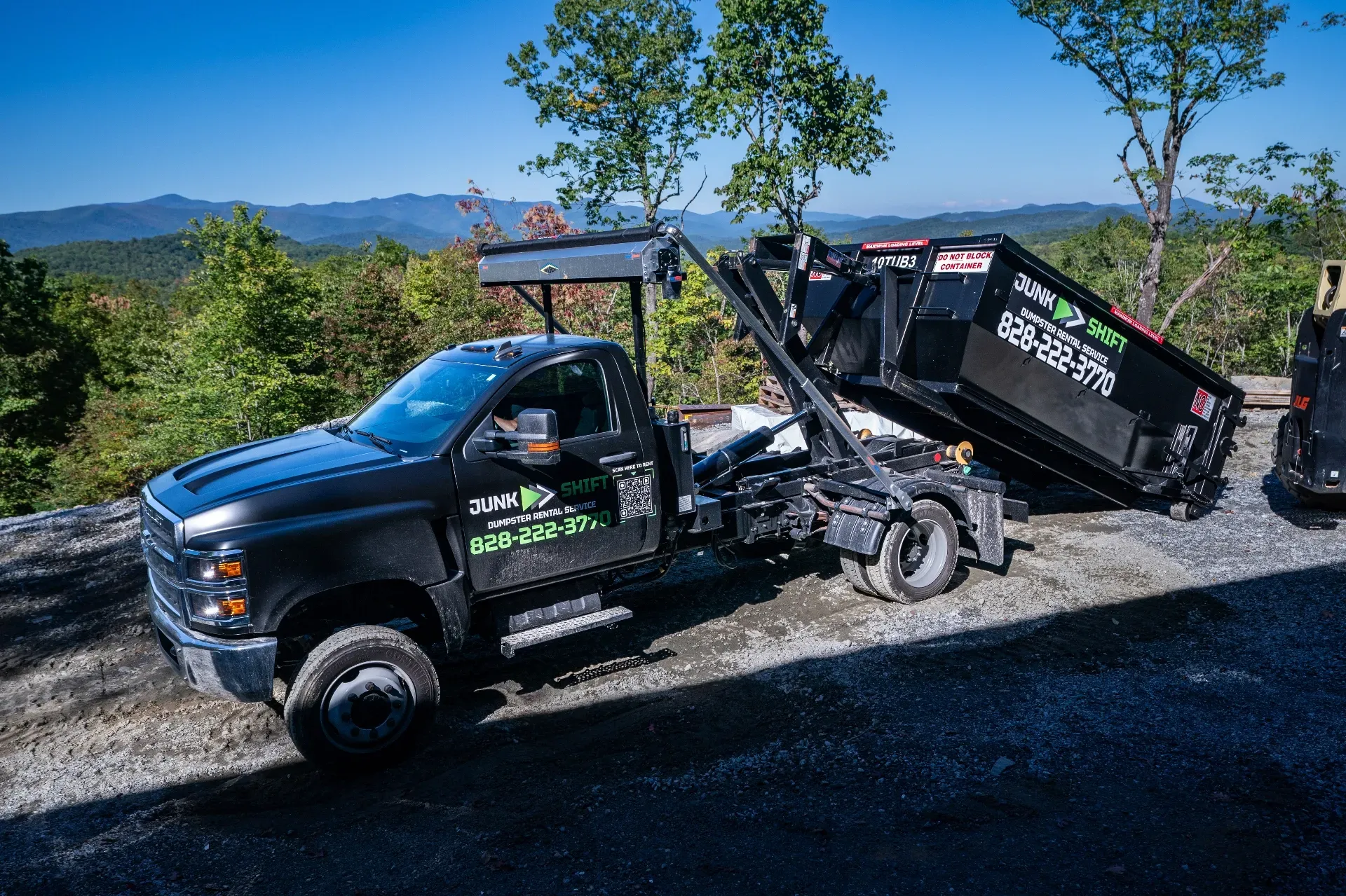 A dumpster is sitting in a gravel lot next to a truck.