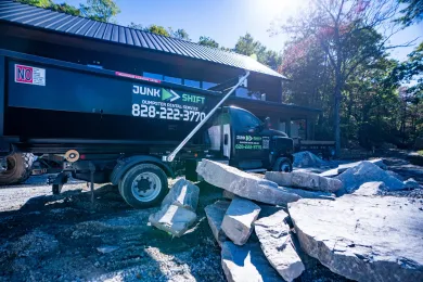 A row of dumpsters are parked in a gravel lot.