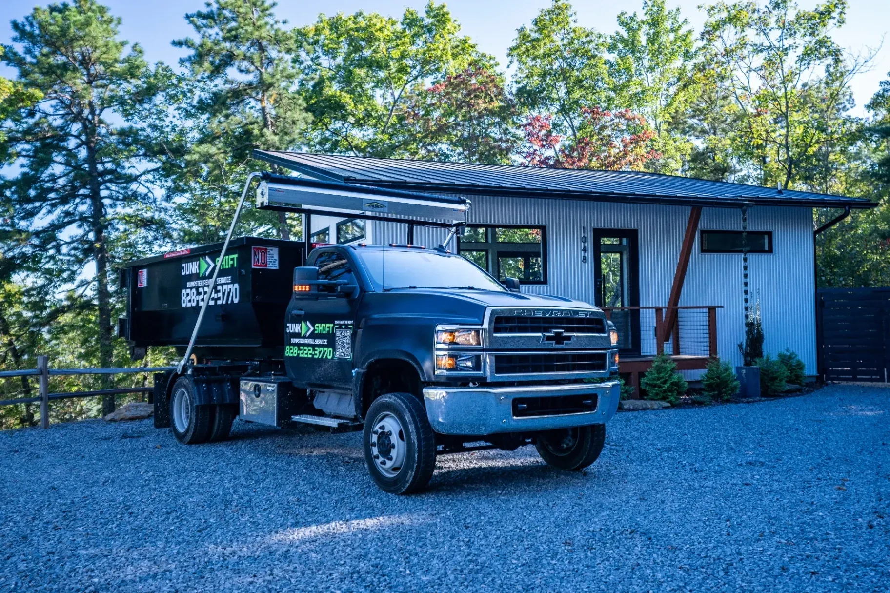 A dumpster is being pulled by a truck on a trailer.