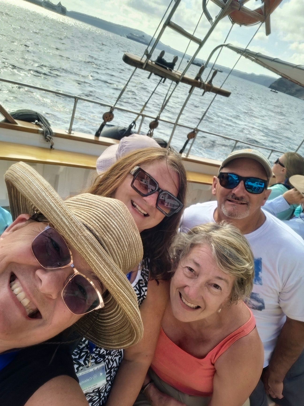 Family of five with backpacks on mountain, arms raised, against a sunny sky.