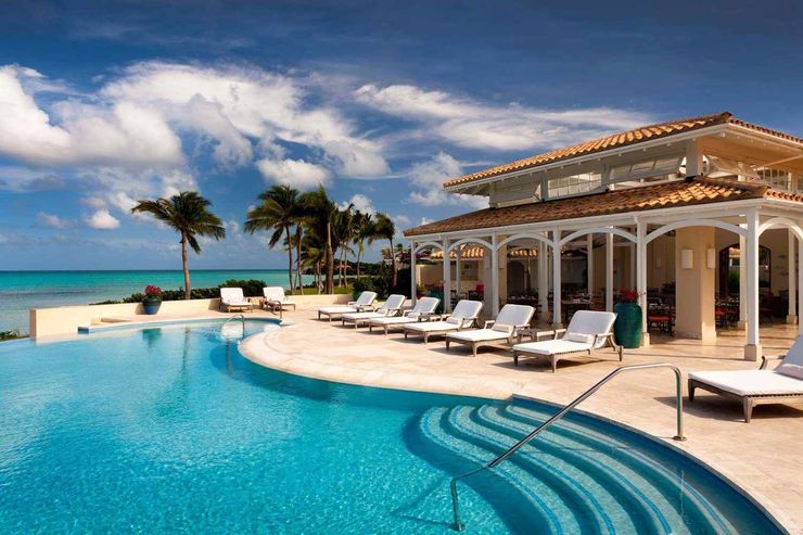 Poolside resort with ocean view, blue water, white lounge chairs, and sunny sky.