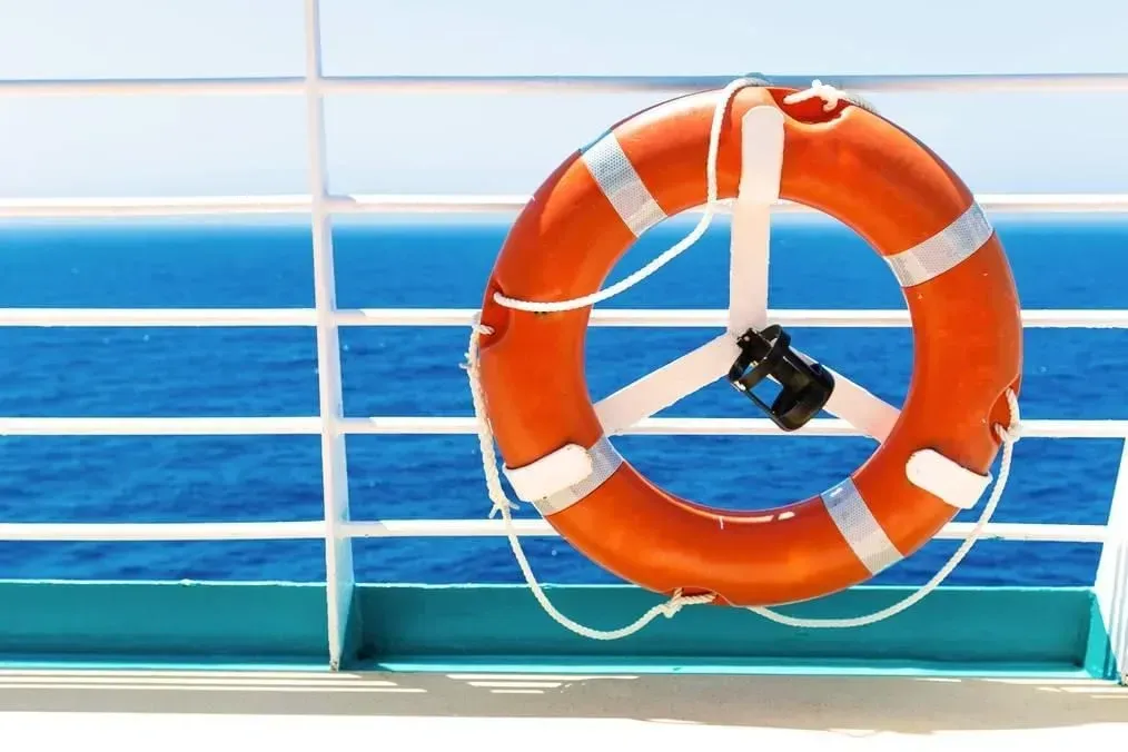 Orange life preserver on a white railing, blue ocean in background.
