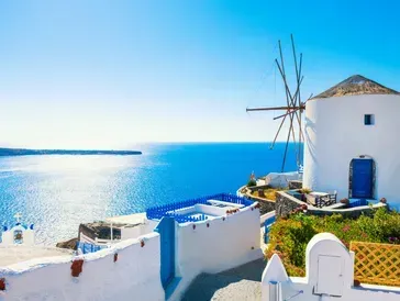 White and blue buildings in Santorini, Greece, with a windmill overlooking the Aegean Sea under a bright blue sky.