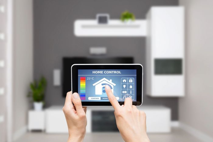 Mani che reggono un tablet che visualizza un'interfaccia di controllo per la domotica in un soggiorno.