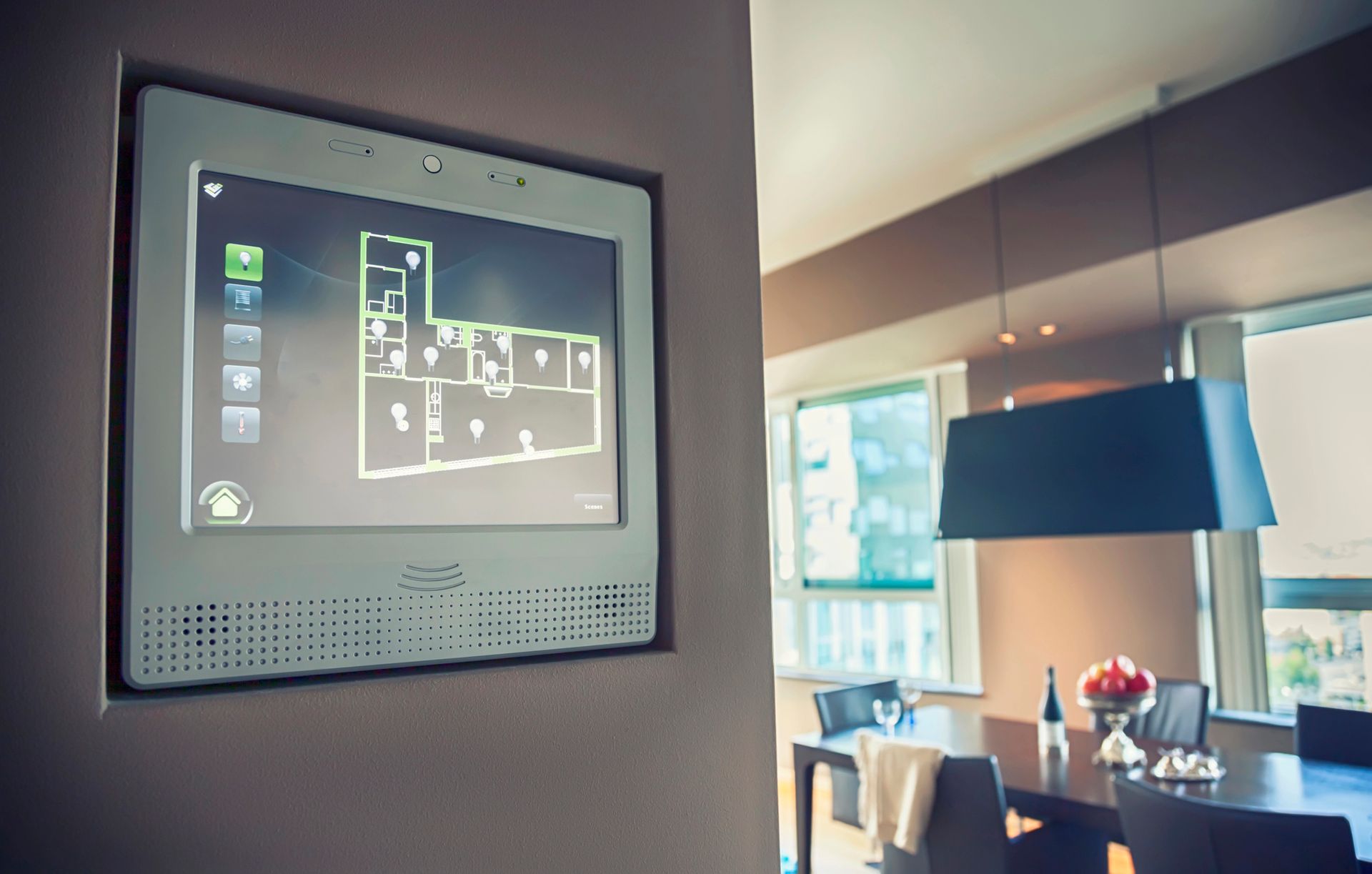 Un pannello di controllo per la casa intelligente, montato su una parete grigia, che mostra la planimetria di una moderna sala da pranzo.