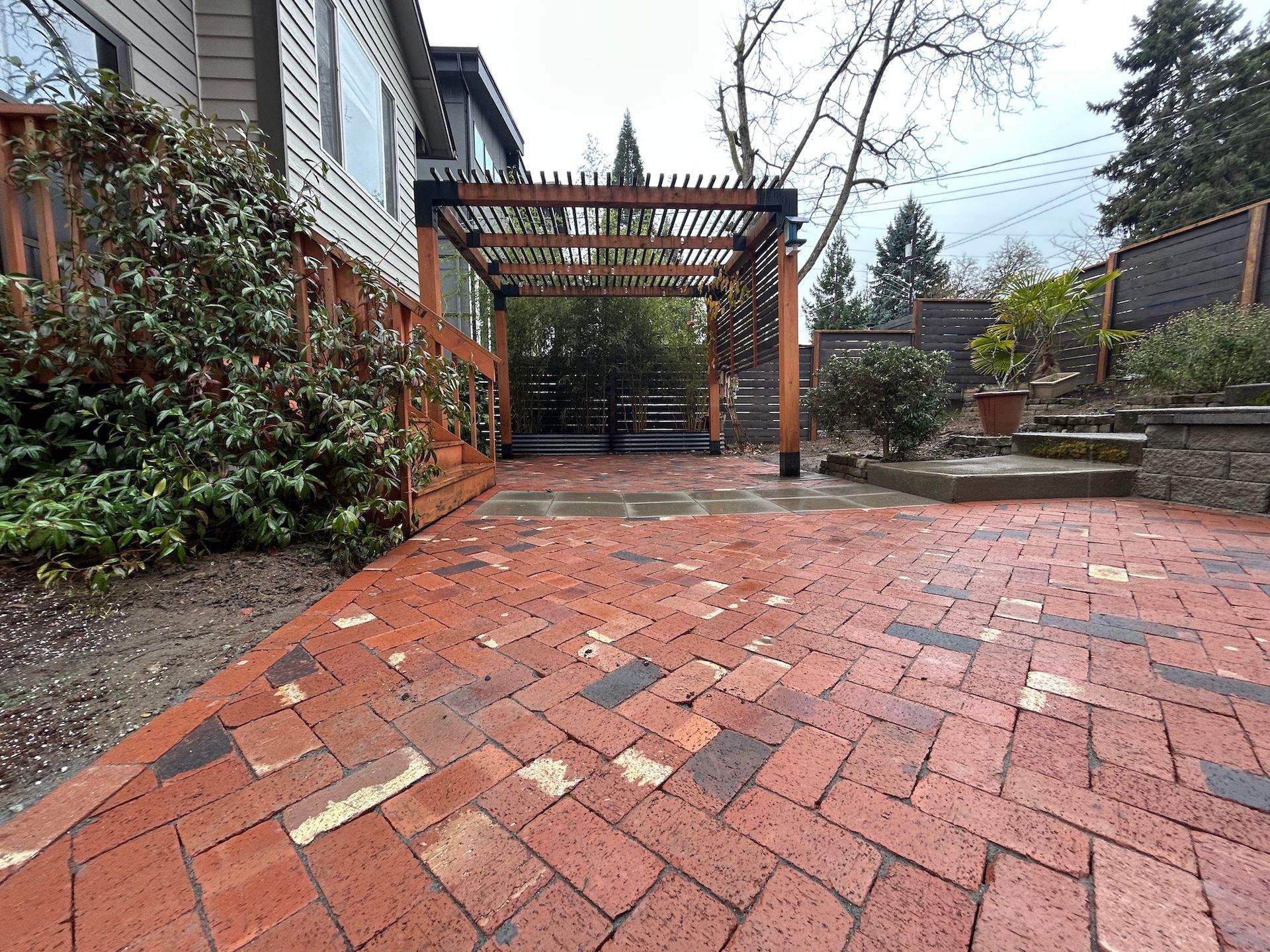 Red brick patio with a wooden pergola and garden path beside a house