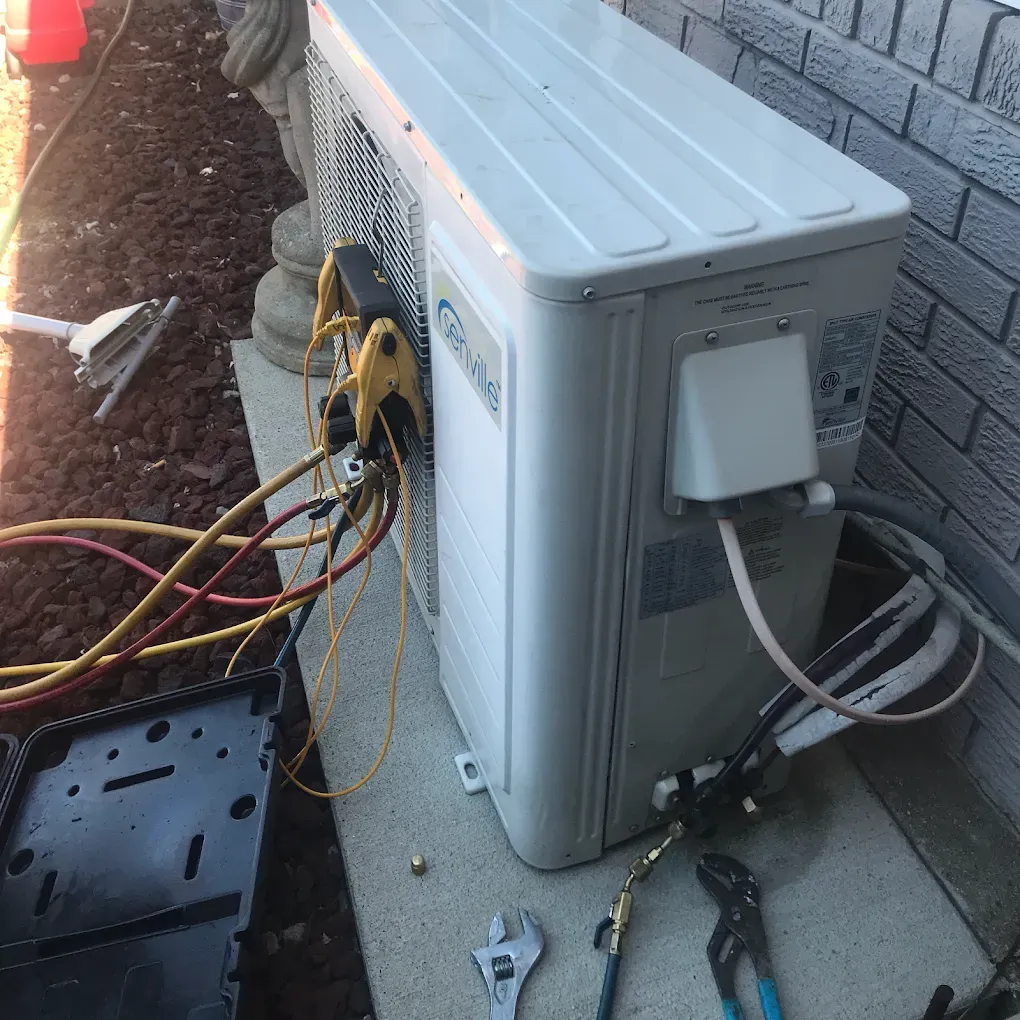 A white air conditioner is sitting on a sidewalk next to a brick wall.