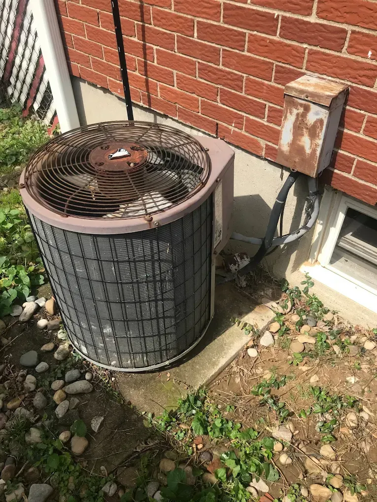 An old air conditioner is sitting on the side of a brick building.