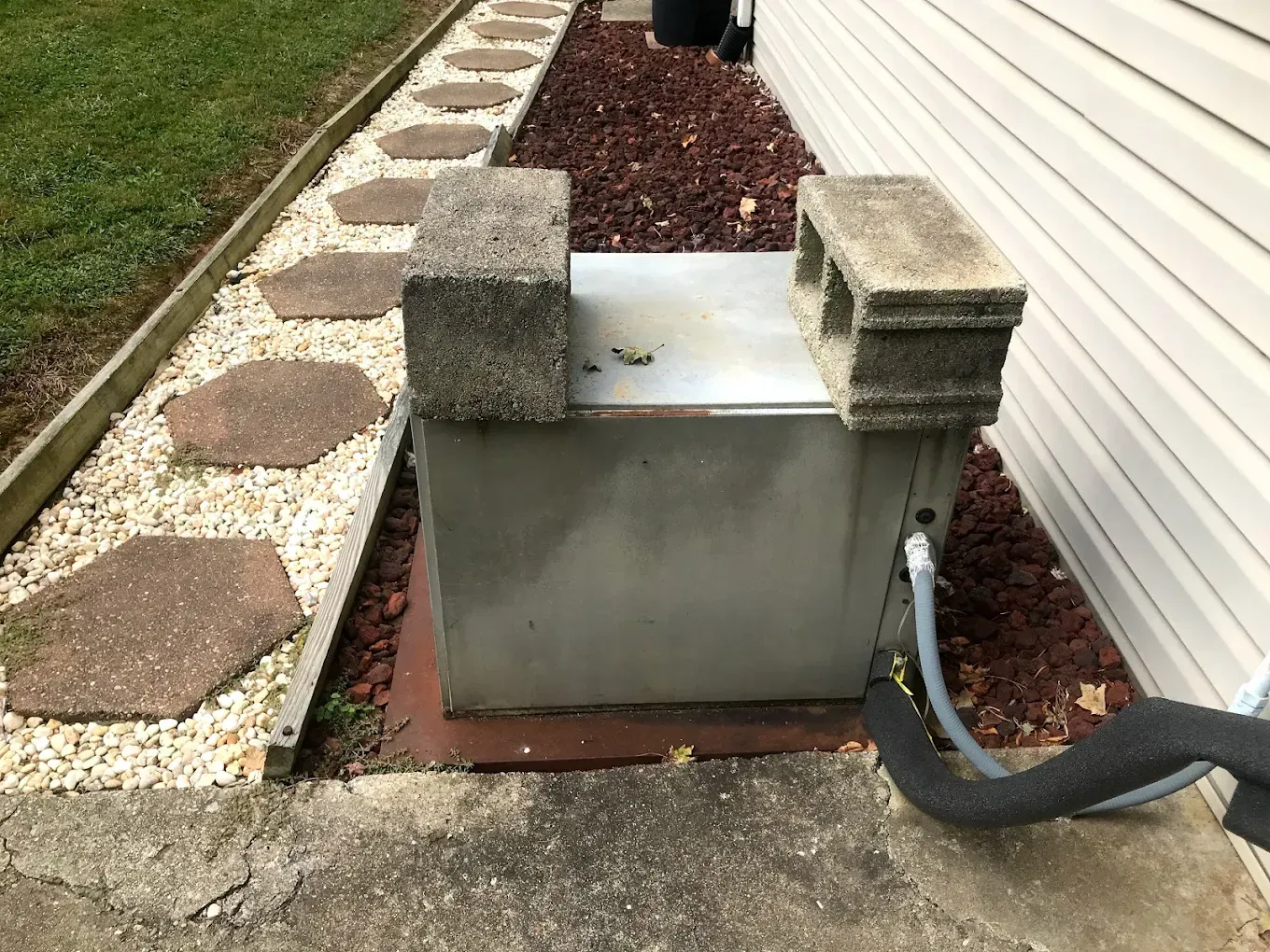 A metal box is sitting on the side of a house next to a sidewalk.