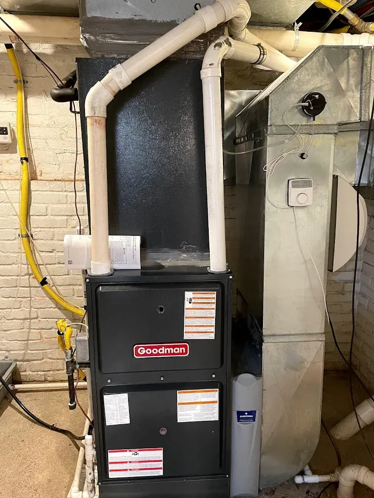 A black furnace is sitting in a basement next to a brick wall.