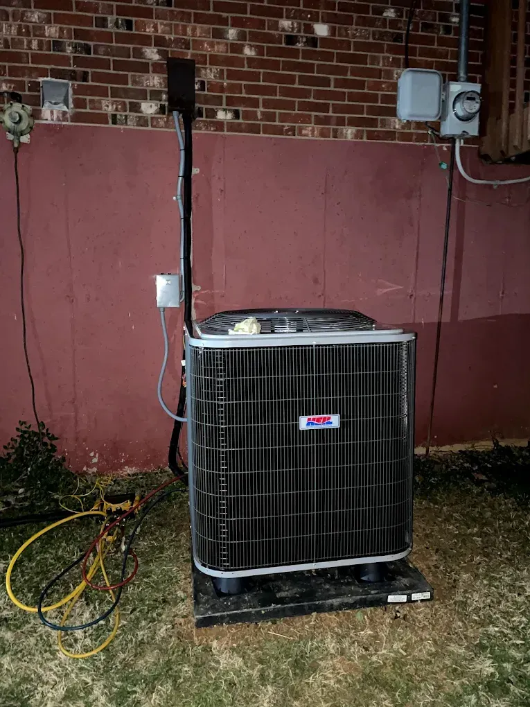 A large air conditioner is sitting in front of a brick wall.