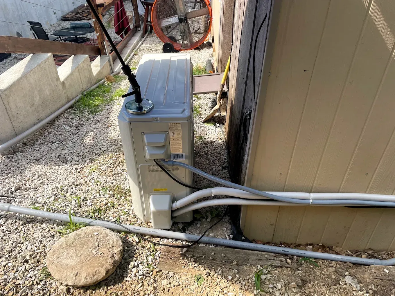 An air conditioner is sitting next to a building with a lot of wires coming out of it.