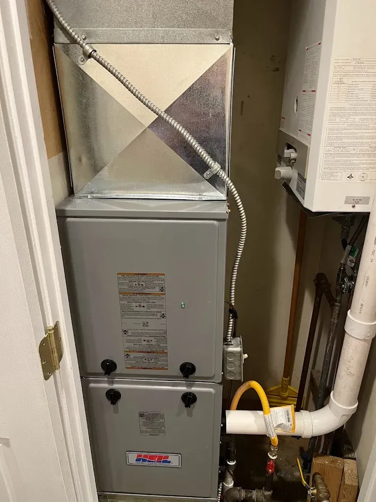 A furnace is sitting in a closet next to a gas heater.