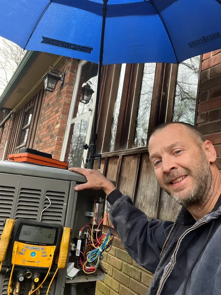 A man is holding an umbrella over an air conditioner.