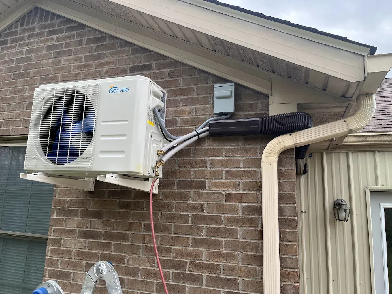 A white air conditioner is mounted on the side of a brick building.