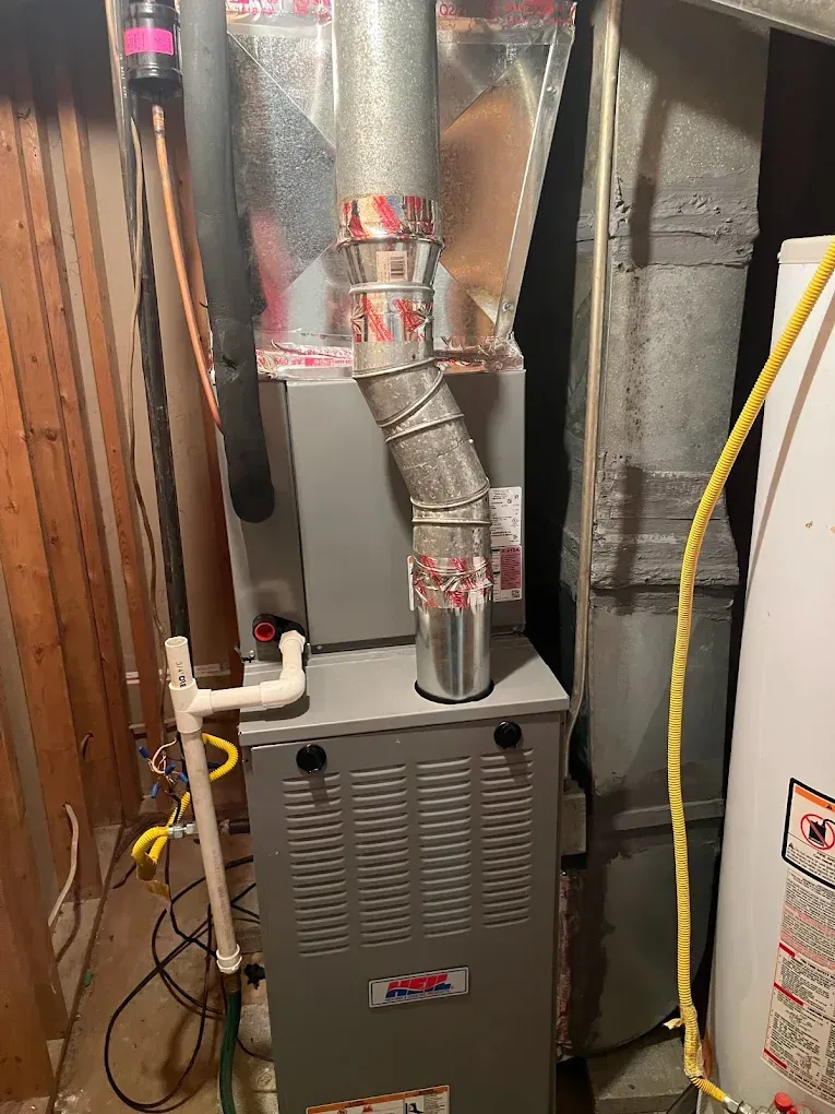 A furnace is sitting in a basement next to a water heater.
