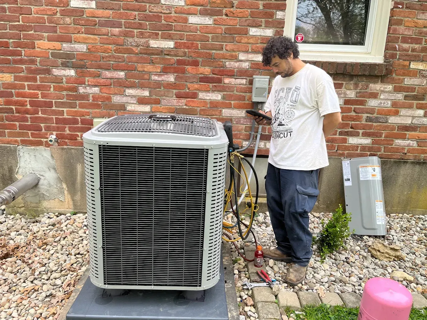 A man is working on an air conditioner outside of a brick building.