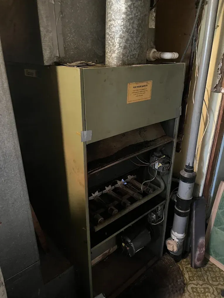 An old heater is sitting in a room next to a pipe.
