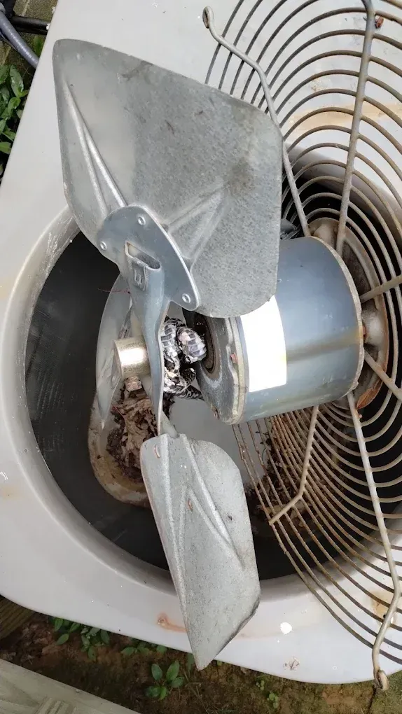 A fan with a broken blade is sitting on top of an air conditioner.