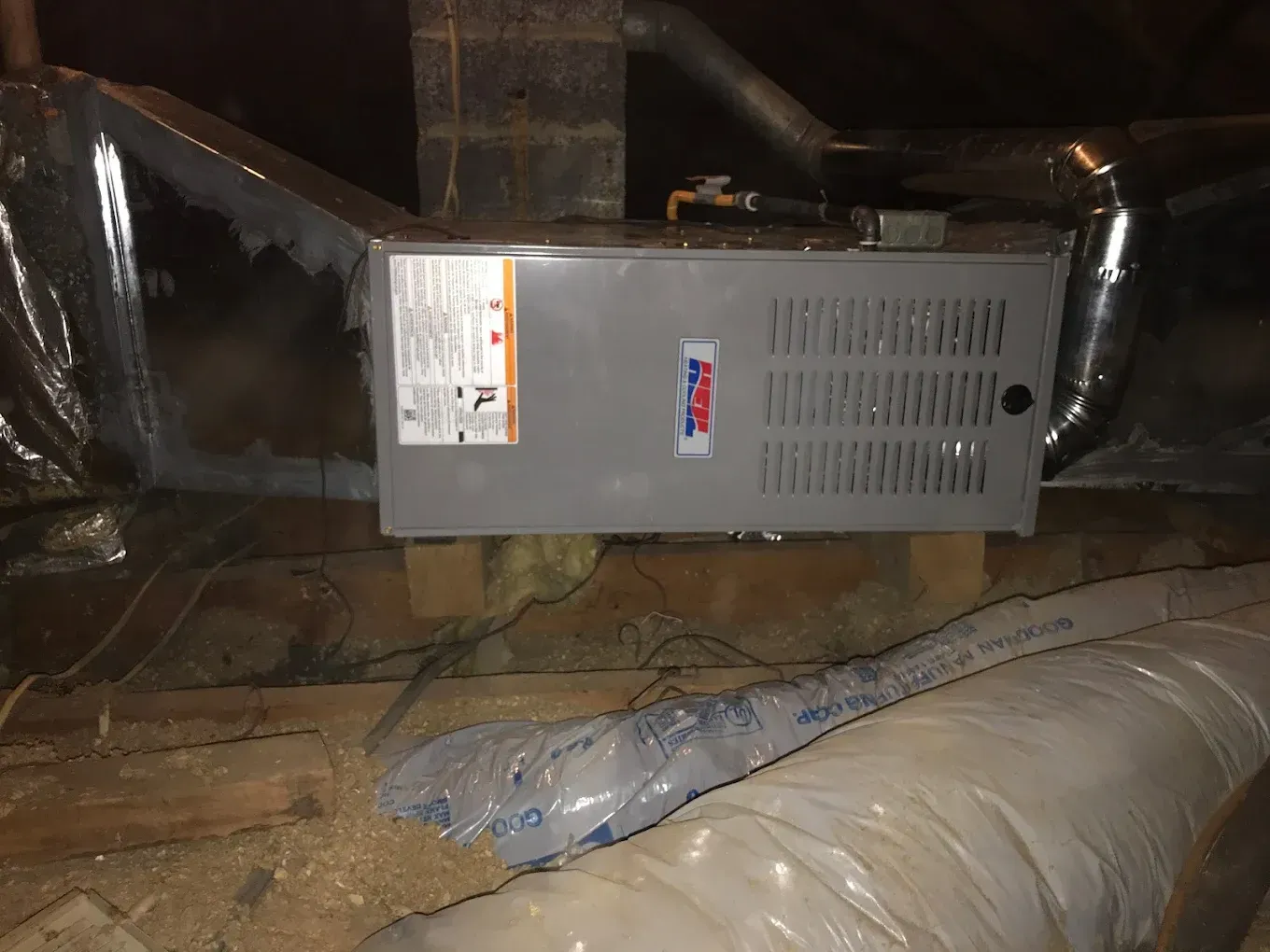 A furnace is sitting in the attic next to a pipe.