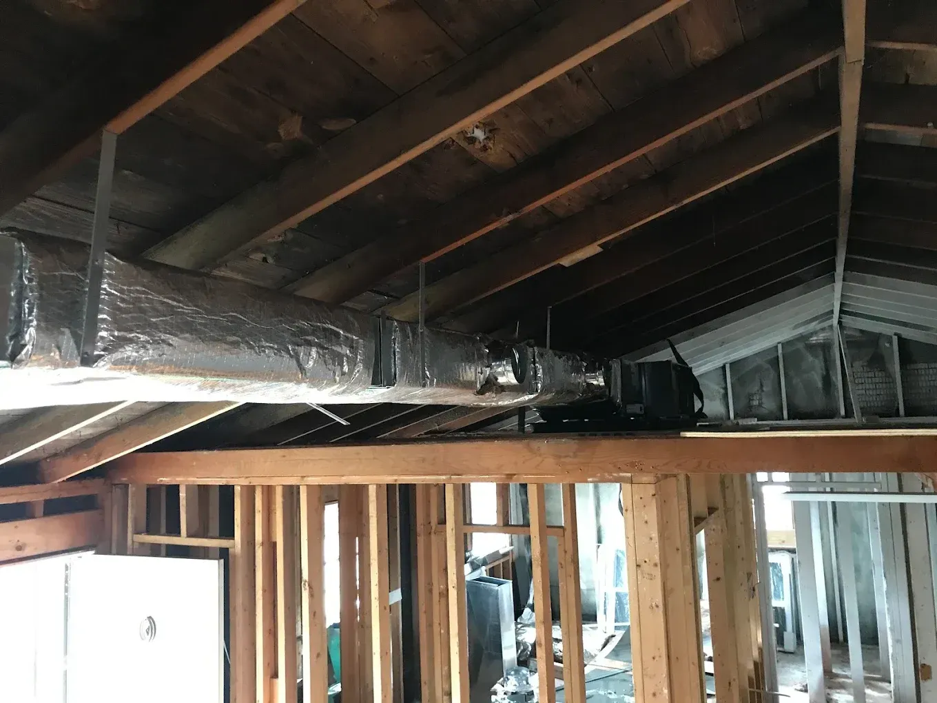A house is being built with a lot of wood and ducts hanging from the ceiling.