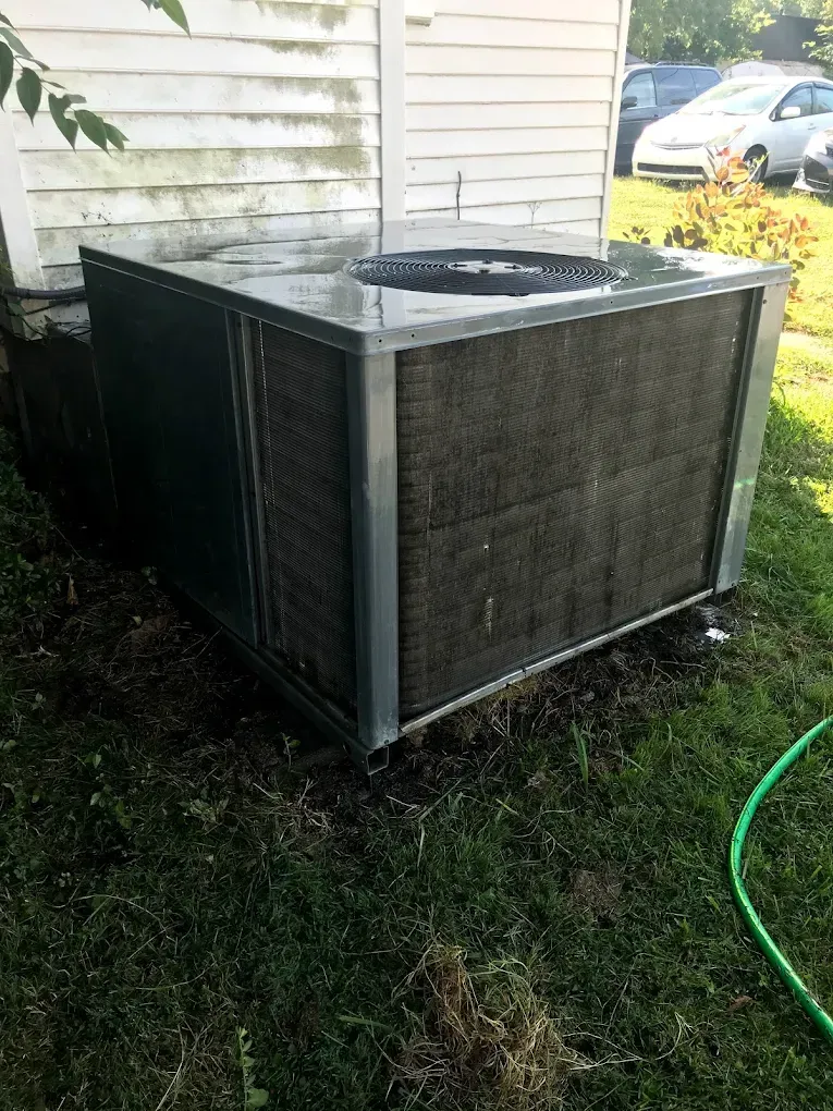 A dirty air conditioner is sitting in the grass next to a house.
