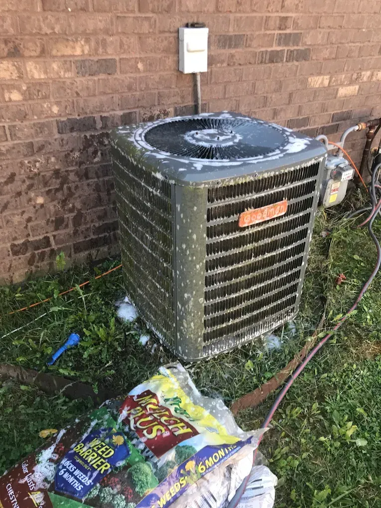 A dirty air conditioner is sitting in the grass next to a bag of dirt.