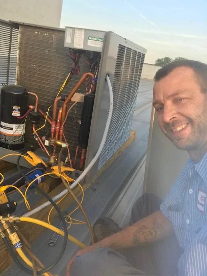 A man is working on an air conditioner on the roof of a building.
