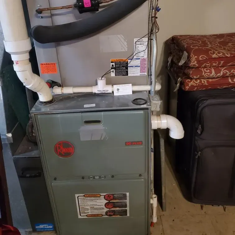 An air conditioner is sitting in a room next to a suitcase.