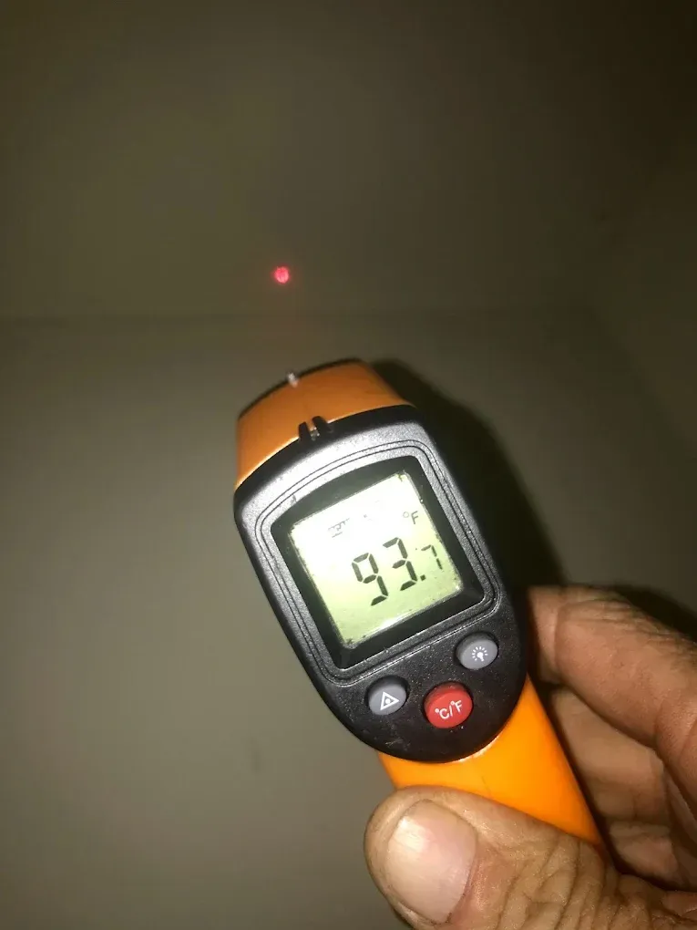A person is holding a digital thermometer with a red light on it.