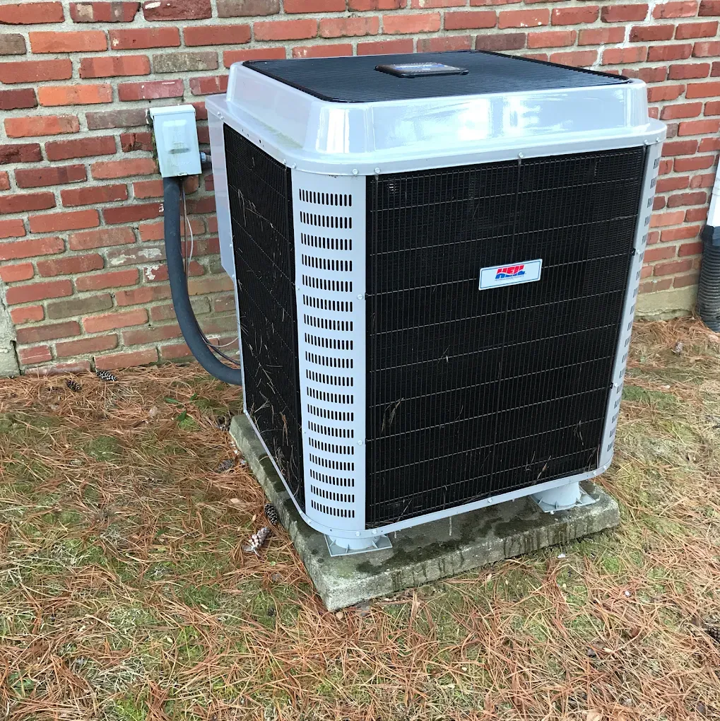 A large air conditioner is sitting outside of a brick building.