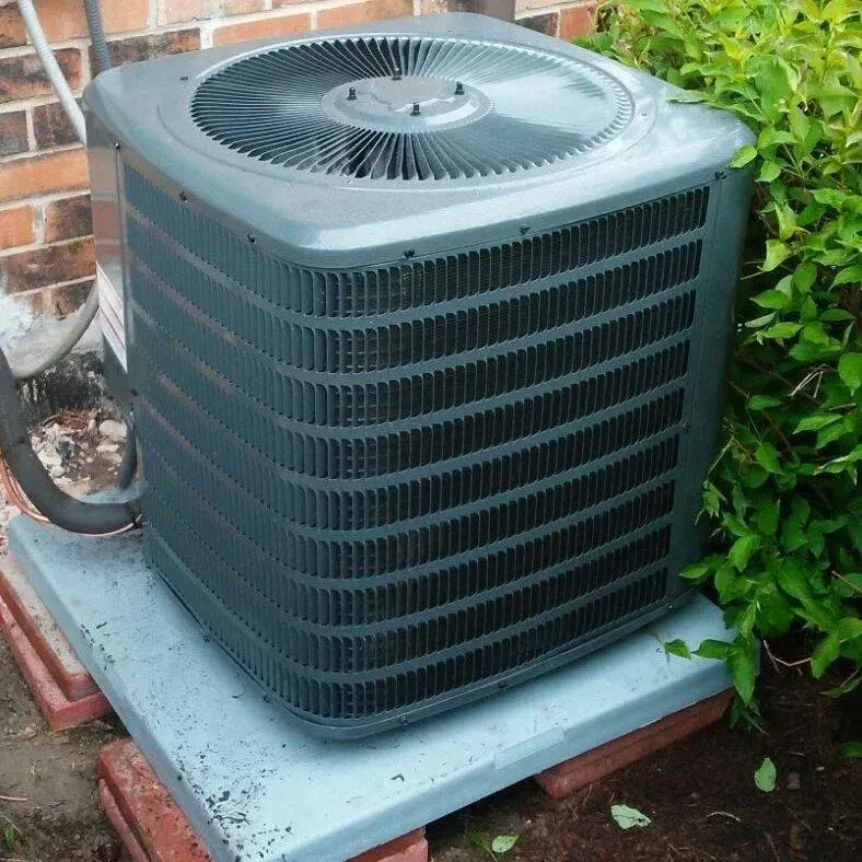 A gray air conditioner is sitting on a brick block