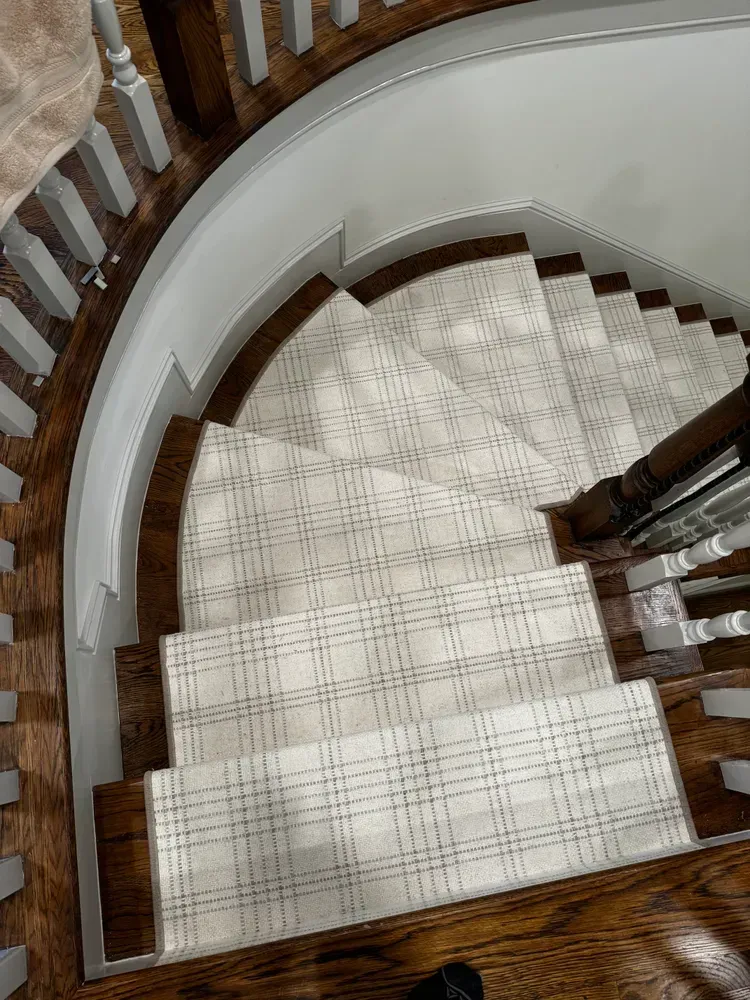 Staircase with a light-colored plaid carpet runner and dark wood railings, viewed from above.