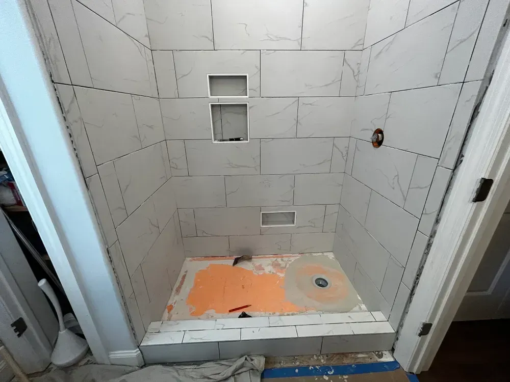 Shower stall in progress, white tile with a niche and plumbing fixtures. Orange mud bed.