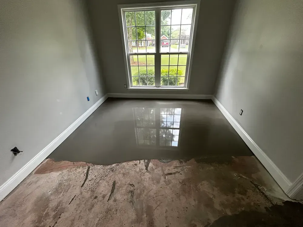 Room with a new, wet concrete floor. Gray walls, white trim, and a window reflecting the outdoors.