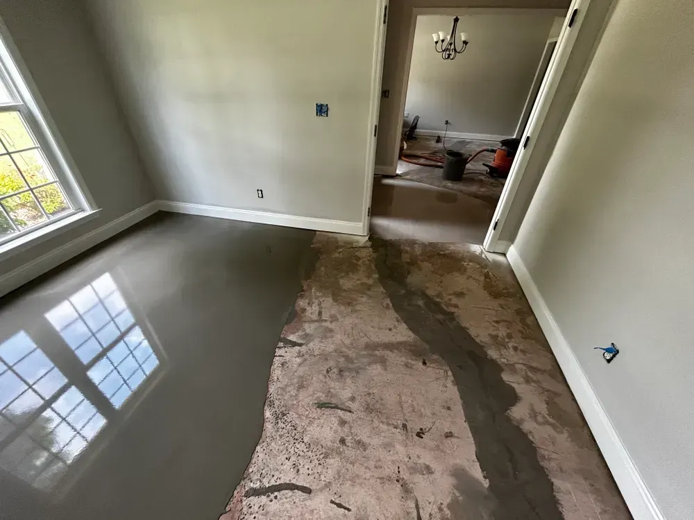 Room with freshly poured gray floor coating, partially covering old brown flooring; doorway to another room.