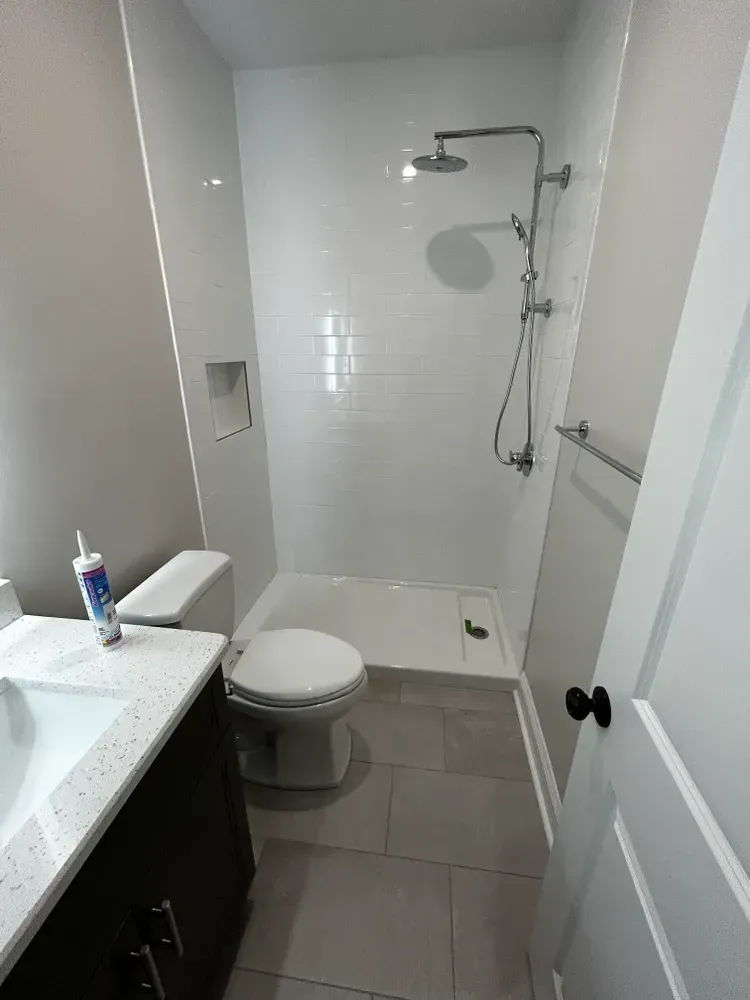Bathroom with white tiled shower, toilet, and vanity with dark brown cabinet.