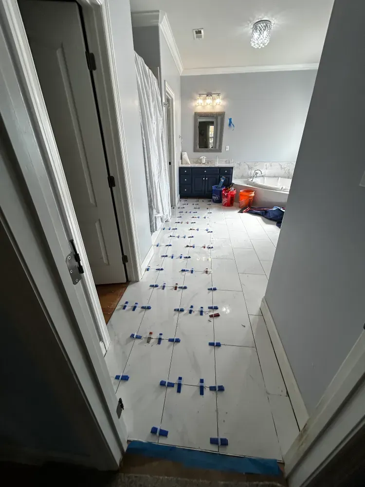 Bathroom floor tile installation in progress. White tiles with blue spacers on a light blue-walled room.