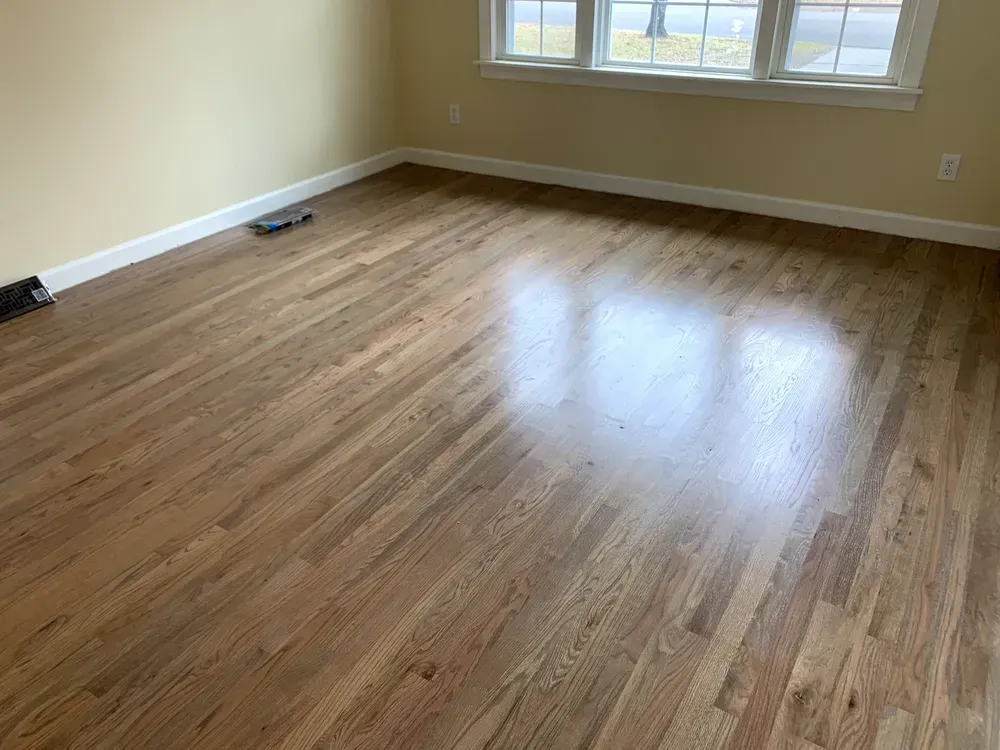 Empty room with glossy hardwood floors, beige walls, and a window.