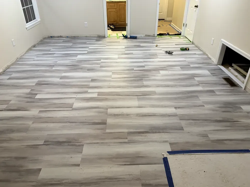 Room with light gray wood-look flooring, walls, and doorways. Construction tools and materials scattered.