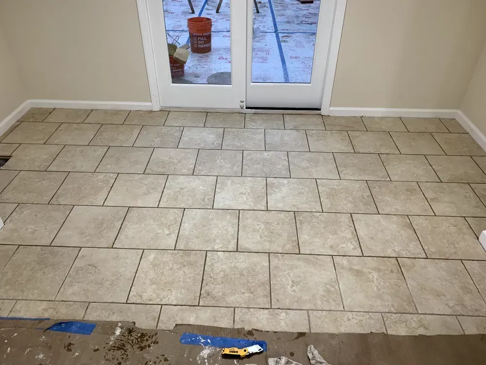 Interior room with beige tiled floor, white door, tan walls. Tiles partially installed.