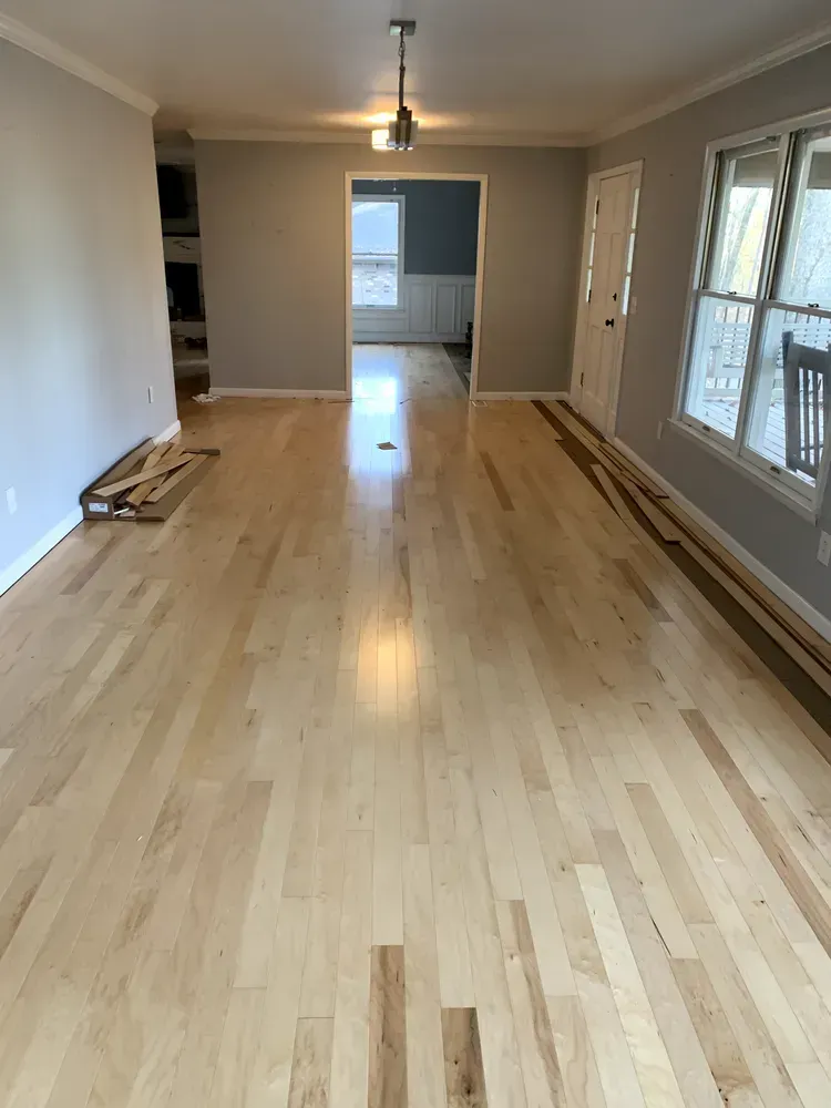 Light wood floor in a house. Gray walls, white trim, and a door are visible.